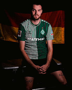 Marvin Ducksch sitzt im Werder-Trikot vor einer Deutschland-Flagge.