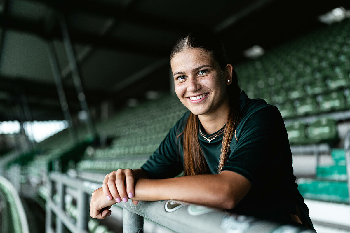 Melina Kunkel lehnt im Stadion über dem Geländer und lächelt in die Kamera.