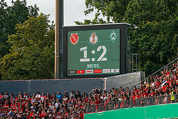 Die ANzeigetafel zeigt 1:2 mit den Logos von Cottbus und Werder.