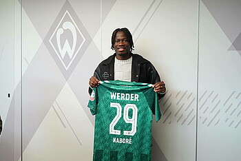 Issa Kaboré holds up a Werder home shirt with the number 29 on the back.