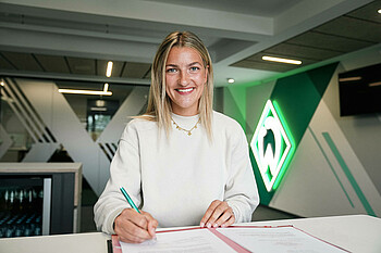 Medina Desic hält einen Stift in ihrer rechten Hand und lächelt in die Kamera.