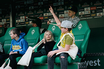 Kinder sitzen auf der Trainerbank im wohninvest Weserstadion.
