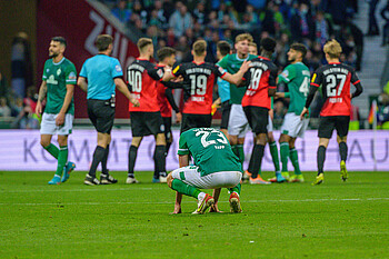 Nicolai Rapp kniet niedergeschlagen, im Hintergrund jubeln Spieler von Holstein Kiel.