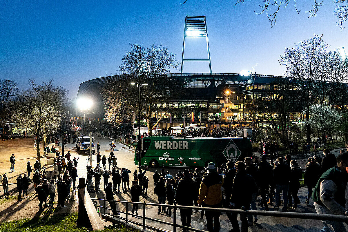 Das erleuchtete wohninvest WESERSTADION mit Mannschaftsbus und Fans.