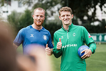 Patrick Zieker und Jens Stage lächeln mit Handball in der Hand in die Kamera.