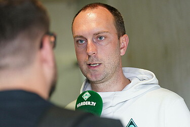 Ole Werner spricht in ein grünes Werder TV Mikrofon. 