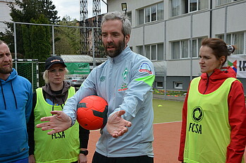 Henrik Oesau Vertreter des SV Werder Bremens erklärt mit einem Ball unter dem Arm 3 Personen eine Übung.