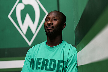 Naby Keïta in front of the Werder logo.