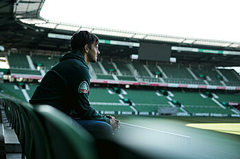 Dawid Kownacki sitting in the stands of the empty wohninvest WESERSTADION.