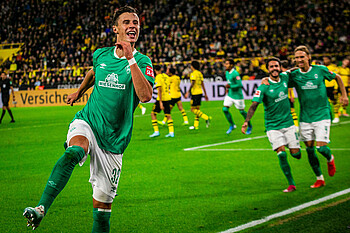 Werder-Spieler Marco Friedl spingt jubelnd, die BVB-Spieler sind im Hintergrund.