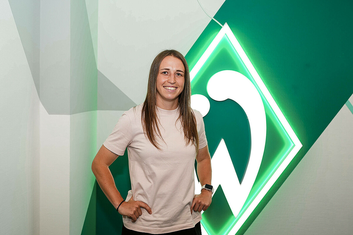 Michaela Specht stützt die Arme in die Hüften und steht vor der Werder-Raute.