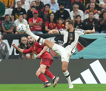 Niclas Füllkrug fährt das Bein aus um einen Ball vor seinem spanischen Gegenspieler zu erreichen.