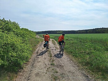 Ein langegezogener Feldweg, auf dem die Radler alle im orangenen Werder Trikot Fahrradfahren. Ein Radler schaut nach hinten in die Kamera.