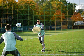 Michael Zetterer im Hintergrund wirft einen Ball in Richtung eines jungen Torhüters, der im Tor steht.