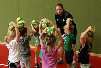 Kinder stehen beim Handball mit der Übungsleiterin im Kreis.
