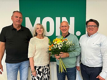 Norbert Sunder bekommt einen Bluemnstrauß überreicht und schaut mit drei weiteren Personen in die Kamera.
