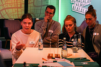 Links im Bild ist Juliane Wirtz zu sehen, welche spricht und mit der einen Hand gestikuliert. Neben ihr steht Tim Barten, Ricarda Walkling und Saskia Matheis
