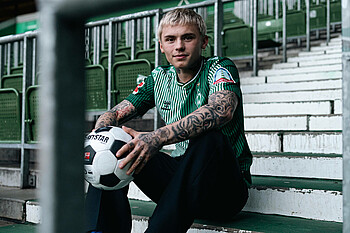 Isak Hansen-Aarøen sitzt mit einem Ball in der Hand auf einer Treppe in der Ostkurve.