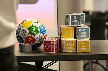 Ein Ball und Papp-Bausteine mit den 17 Nachhaltigkeitszielen stehen auf einem Tisch