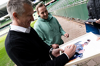 Frank Baumann unterzeichnet das gemeinsame Foto mit Fan Hannes Schwabe. 