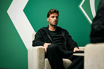 Olivier Deman sitzt in einem Sessel, im Hintergrund ist eine grüne Wand.