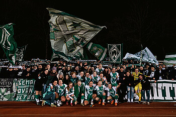 Mannschaftsfoto vor der Tribüne wo die Ultras mit Fahnen stehen.