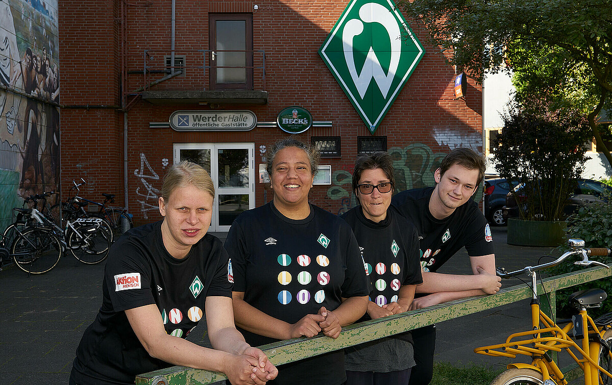 Vier Athlet:innen lehnen mit Inklusionsshirts an einer Ballustrade vor der Werder-Halle.