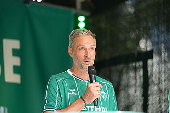 Tarek Brauer im Werder-Heimtrikot am Mikro. 