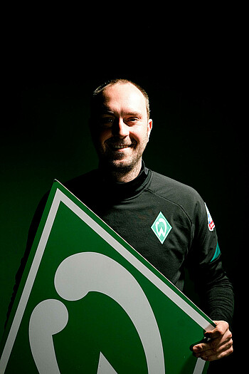 Cheftrainer Ole Werner mit einem großen Werder-Emblem in der Hand