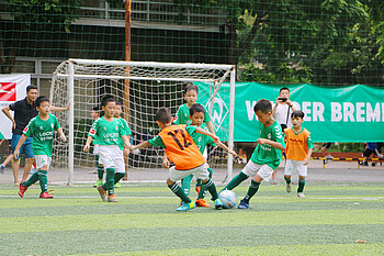Kinder in grünen Trikots spielen Fußball.