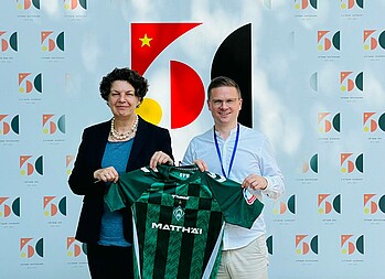 Helga Margarete Barth and Dominik Kupilas hold up a Werder shirt.