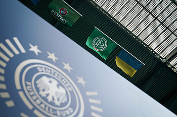 Die Flagge der Ukraine neben der DFB-Flagge hoch oben im Stadion aufgehängt. Im Vordergrund das DFB-Logo im Stadion auf einer Bande.