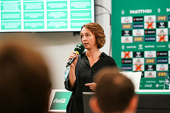 Anne-Kathrin Laufmann hält ein Mikrofon in der Hand und spricht zum Publikum.