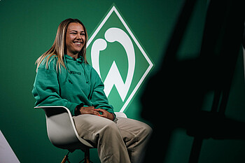 Maja Sternad sitzt auf einem Stuhl vor der Werder-Raute