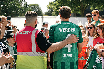 Ein Ordner begleitet Niklas Stark durch die Menschenmenge. Sie sind von hinten zu sehen