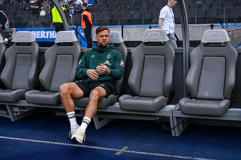 Niclas Füllrug sitzt alleine auf der Auswechselbank im Berliner Olympiastadion. Er trägt einen grünen Pullover.
