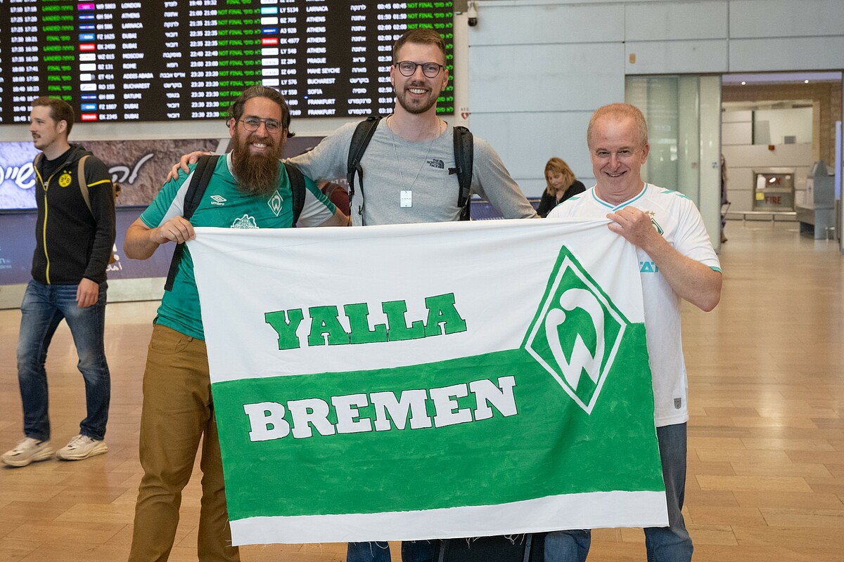Arne Scholz mit zwei Fans, die eine Fahne mit der Aufschrift "Yalla Bremen" zeigen". 