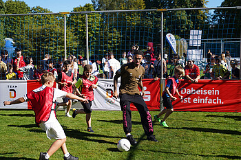Justin Njinmah spielt mit ein paar Schüler:innen Fußball.