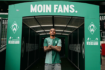 Justin Njinmah steht vor dem Spielertunnel mit der Aufschrift "Moin Fans".