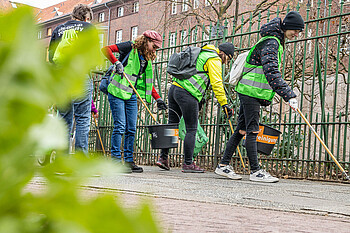 Menschen sammeln Müll an einem Zaun