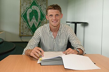Jens Stage unterschreibt seinen Vertrag und lächelt