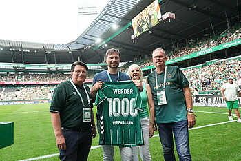 Gruppenbild mit Trikotübergabe auf dem Rasen des Weserstadions vor vollen Tribünen in der Halbzeit. 