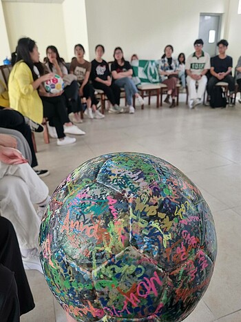 Ein Ball mit tausenden Unterschriften im Vordergrund, im Hintergrund sind die Teilnehmer:innen des Workshops zu sehen.