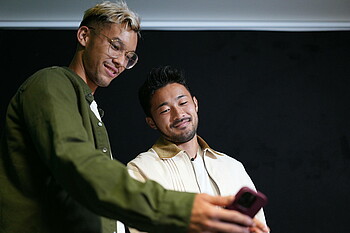 Yukinari Sugawara und Mio Backhaus schauen in ein Smartphone