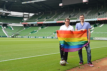 Dr. Hubertus Hess-Grunewald und Robert Dadanski halten eine Regenbogenfahne hoch.