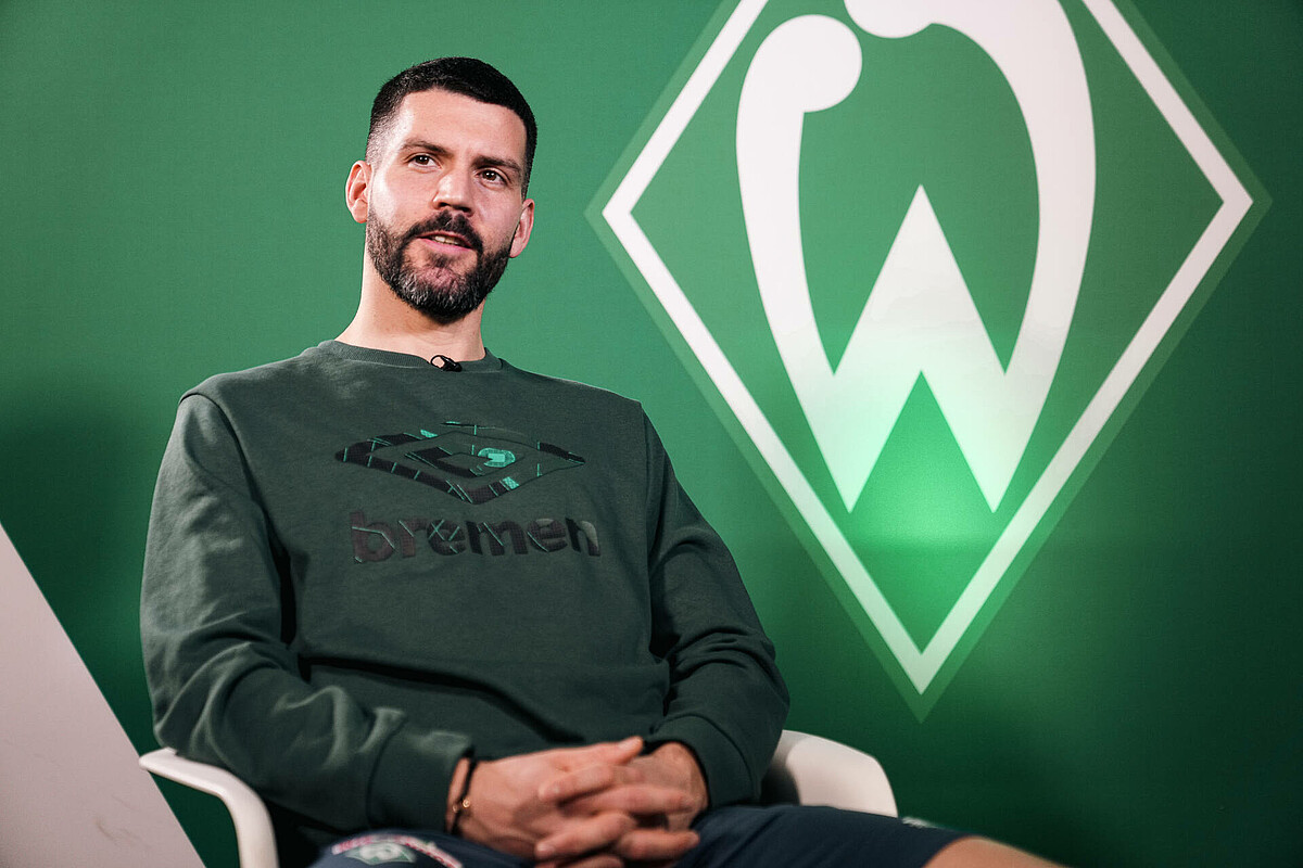 Anthony Jung sitting on a chair for the Interview - the Werder logo is in the background