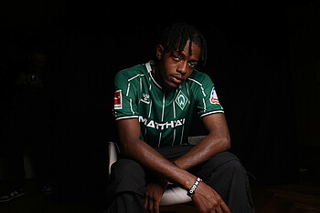 Mbangula sitting on a chair while wearing a Werder shirt.