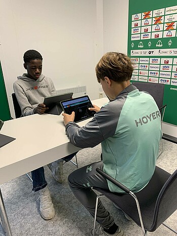 Zwei Spieler sitzen am Tisch mit den Tablets vor sich.