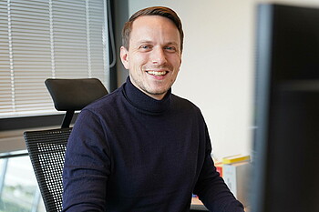 Dr. Henning Hofmann sitzt in seinem Büro und lächelt in die Kamera