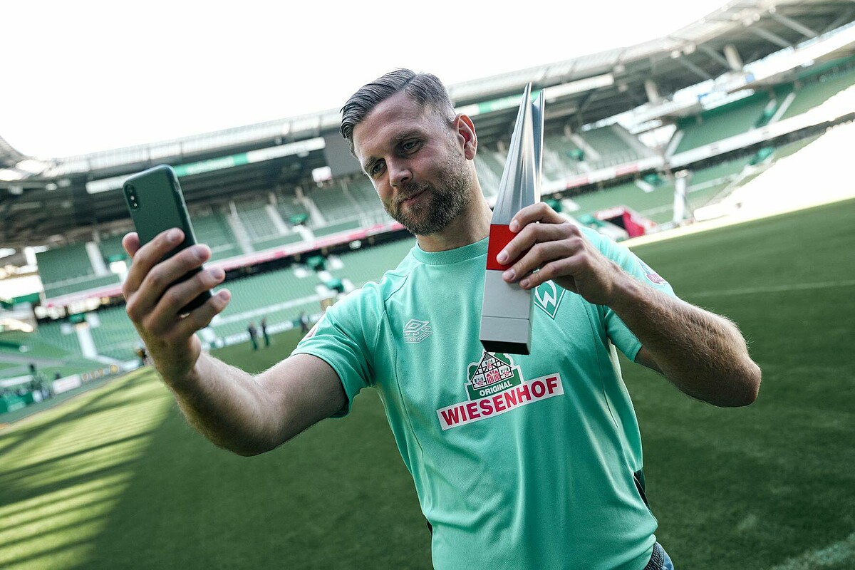 Füllkrug macht ein Selfie mit der Trophäe zum Spieler des Monats der Bundesliga.